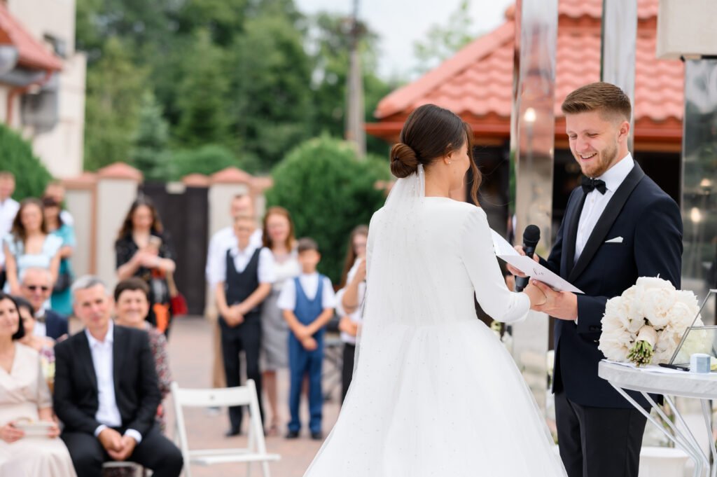 side view smiling groom man with microphone holding bride s hand swears oath wedding ceremony outdoors happy guests background enjoying beautiful couple elegant wife puffy dress
