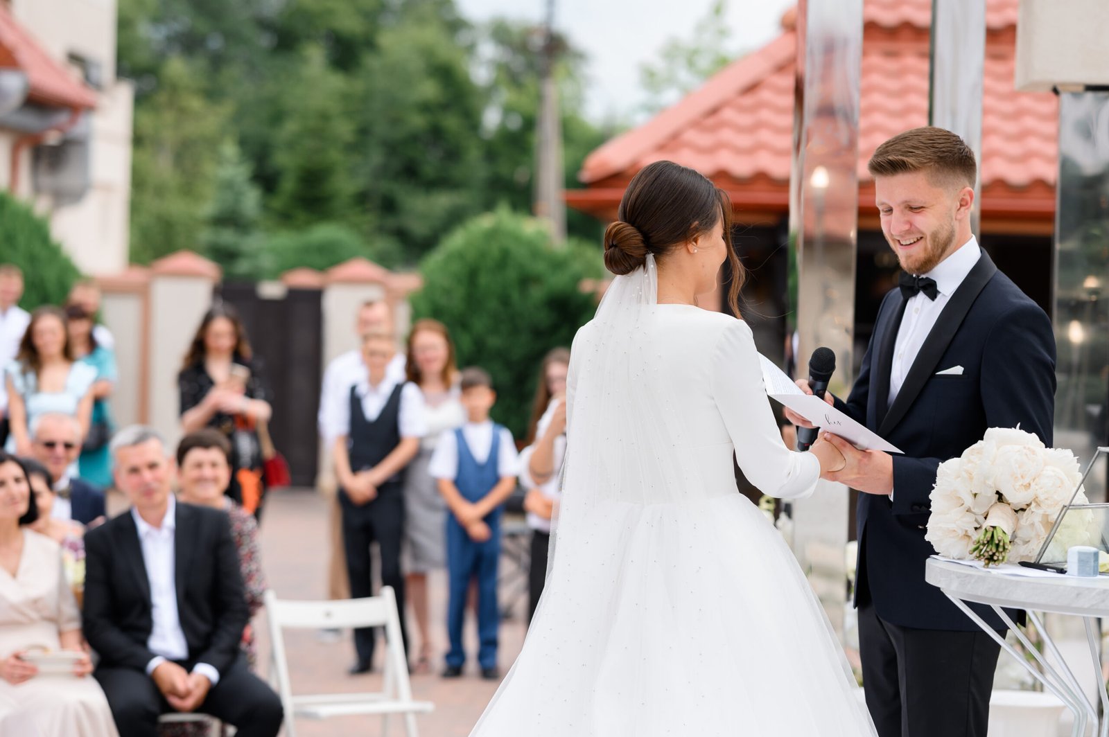 side view smiling groom man with microphone holding bride s hand swears oath wedding ceremony outdoors happy guests background enjoying beautiful couple elegant wife puffy dress